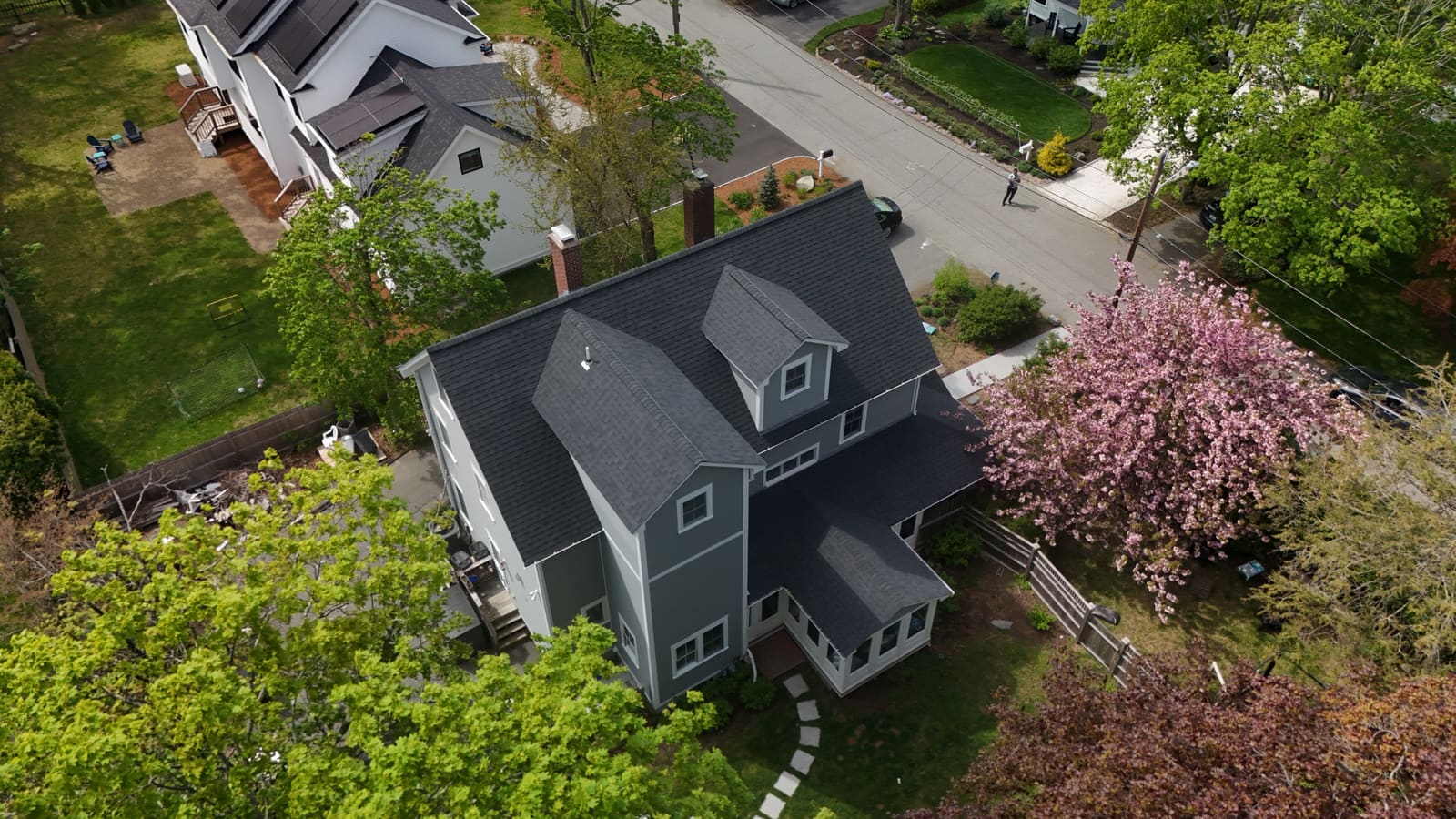 Gray house with a dark asphalt shingle roof beside a flowering tree