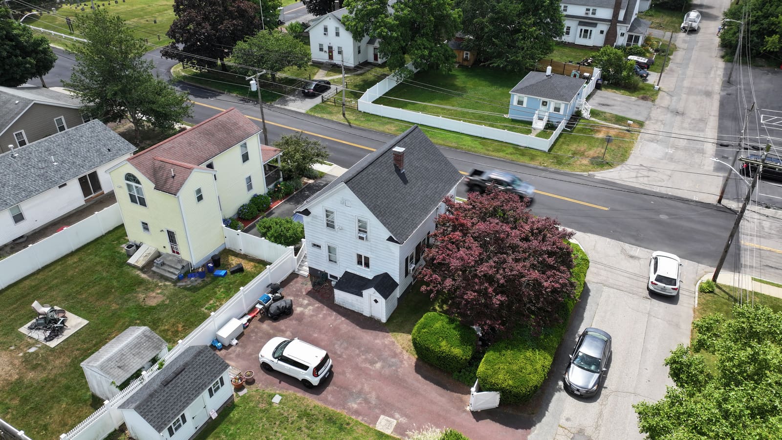 White house with a dark shingle roof on a corner lot seen from above