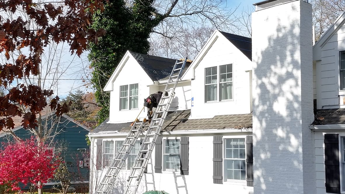 Roofer on a ladder repairing shingles at a dormer